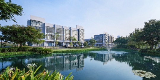 Modern university campus buildings along a reflective pond with a fountain and trees behind them.