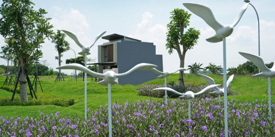 Modern house in the distance with a manicured lawn, purple flowers, and white metal bird sculptures in the foreground.