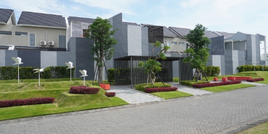 Row of modern gray townhouses with a gated entrance, manicured lawns, and trees along a paved street.